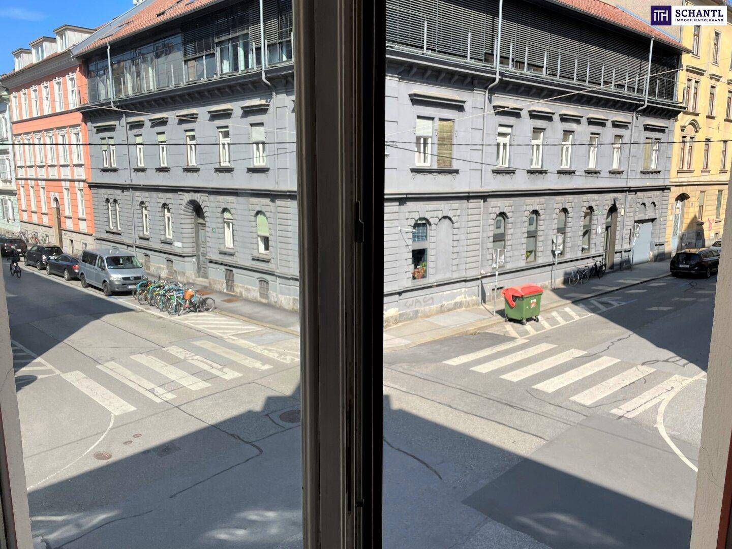 Blick aus dem Fenster auf eine belebte Straßenkreuzung mit umliegenden Gebäuden und Fahrzeugen.