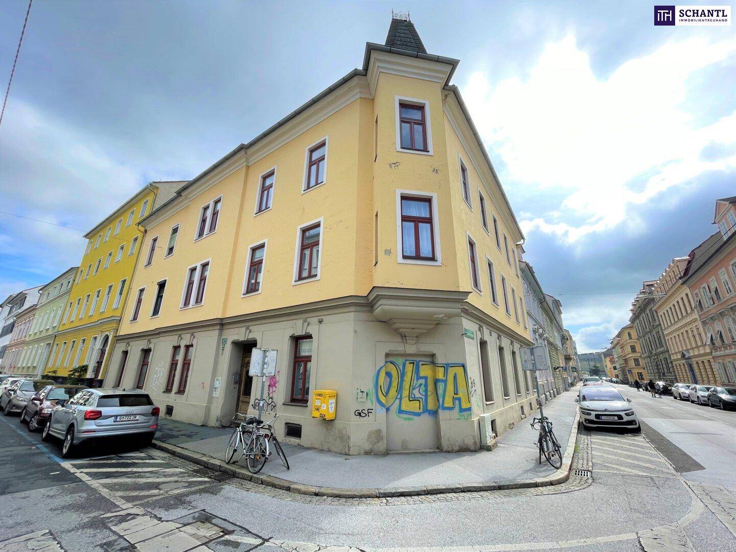 Eckgebäude mit gelber Fassade, vielen Fenstern und parkenden Autos an der Straße.