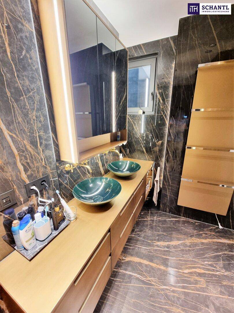 Luxuriöses Badezimmer mit dunklen Marmorwänden, Holzwaschtisch, zwei grünen Aufsatzwaschbecken und Fenster.