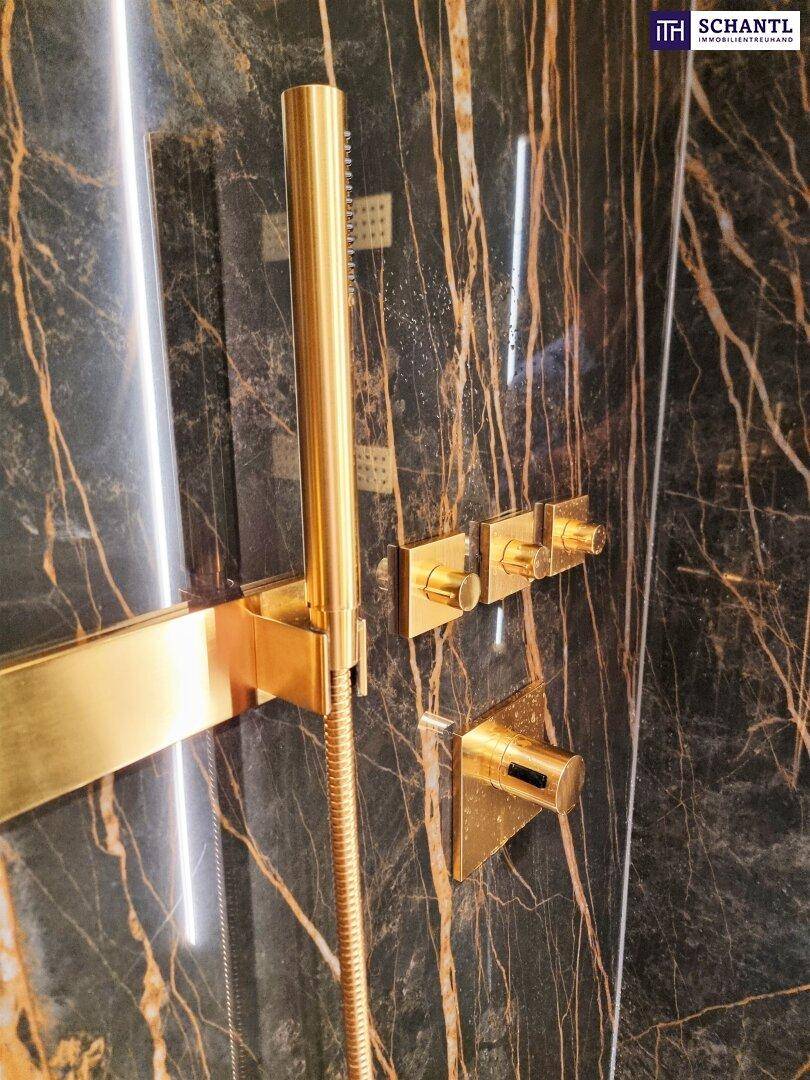 Goldene Duscharmatur und Brausekopf an einer eleganten Wand aus dunklem Marmor.