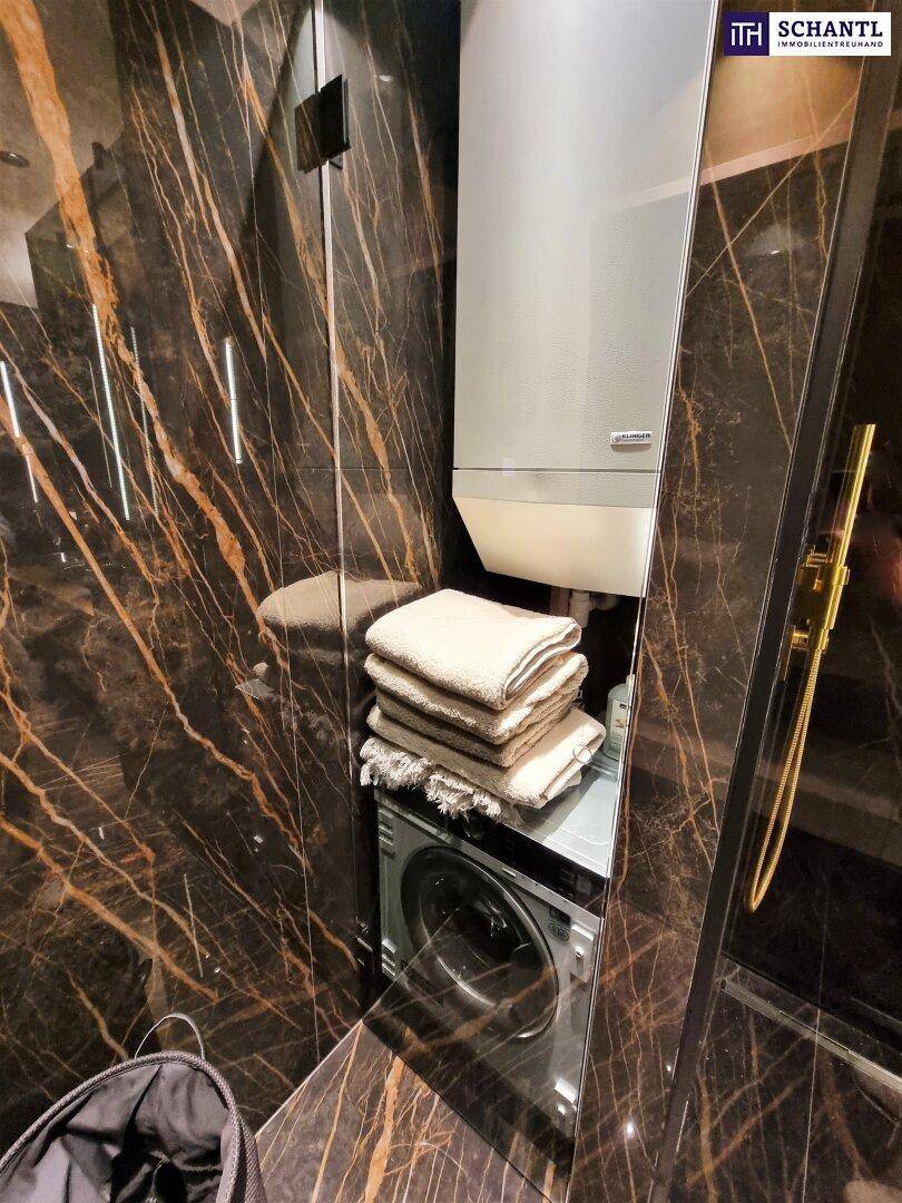 Praktischer Waschbereich mit Waschmaschine und Warmwasserbereiter, umgeben von dunklen Marmorwänden.