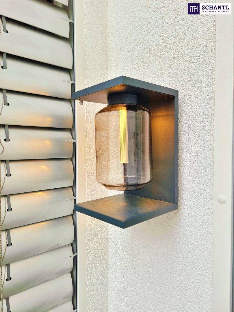 Moderne Wandleuchte an der Außenfassade neben einem Fenster mit Rollläden.