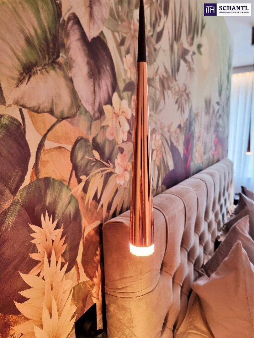Schlafzimmer mit großem gepolstertem Kopfteil, moderner Pendelleuchte und tropischer Blumentapete.