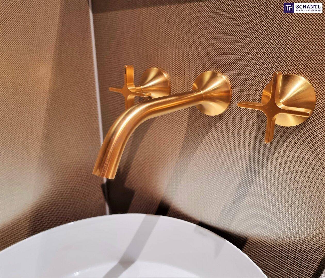 Moderne goldene Armatur und Wandhahn über einem eleganten Waschbecken in einem Badezimmer.