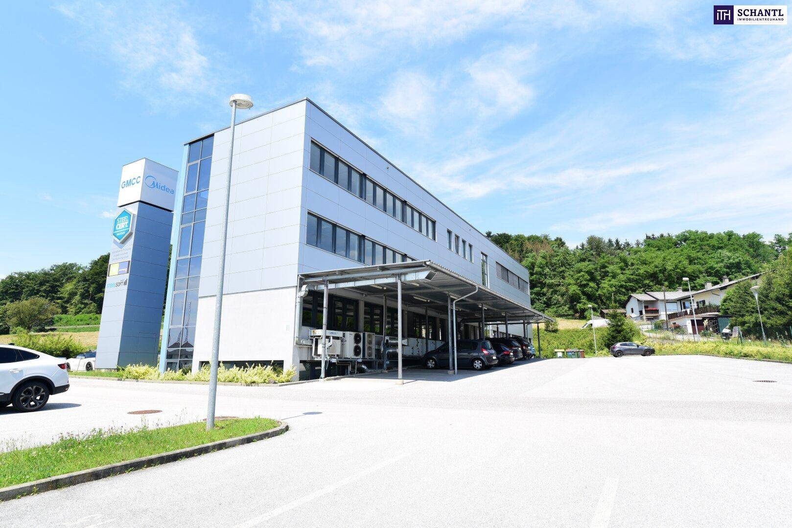 Seitenansicht des Bürogebäudes mit überdachten Parkplätzen und weitem Blick ins Grüne.