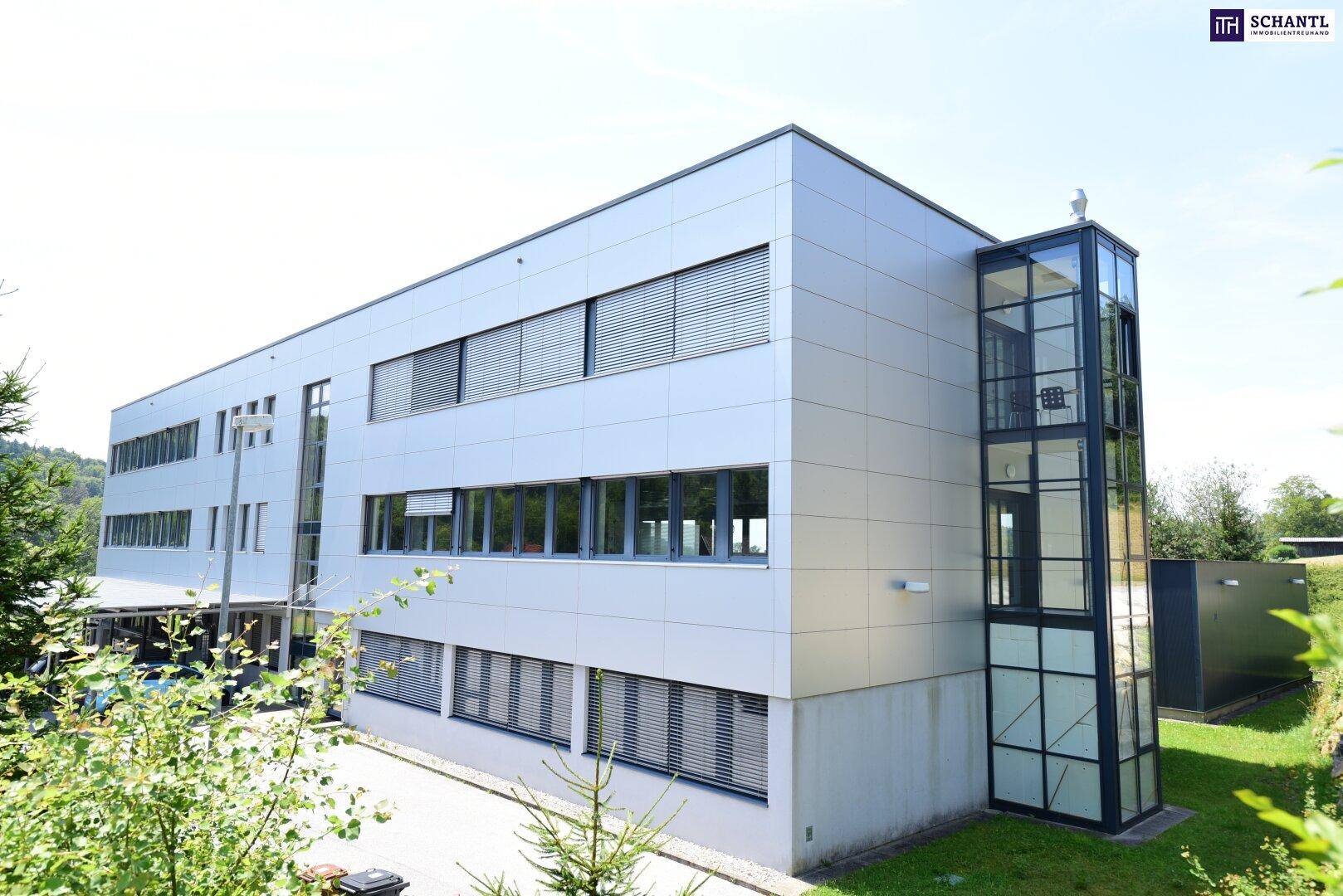 Rückansicht des Bürogebäudes mit externem Glasaufzug und modernen Fensterfronten.