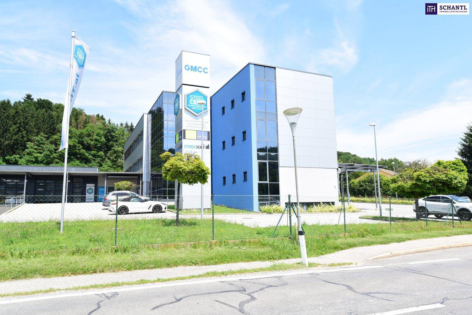 Ansicht des modernen Bürogebäudes mit blauer Glasfassade und Beschilderung, umgeben von Bäumen.