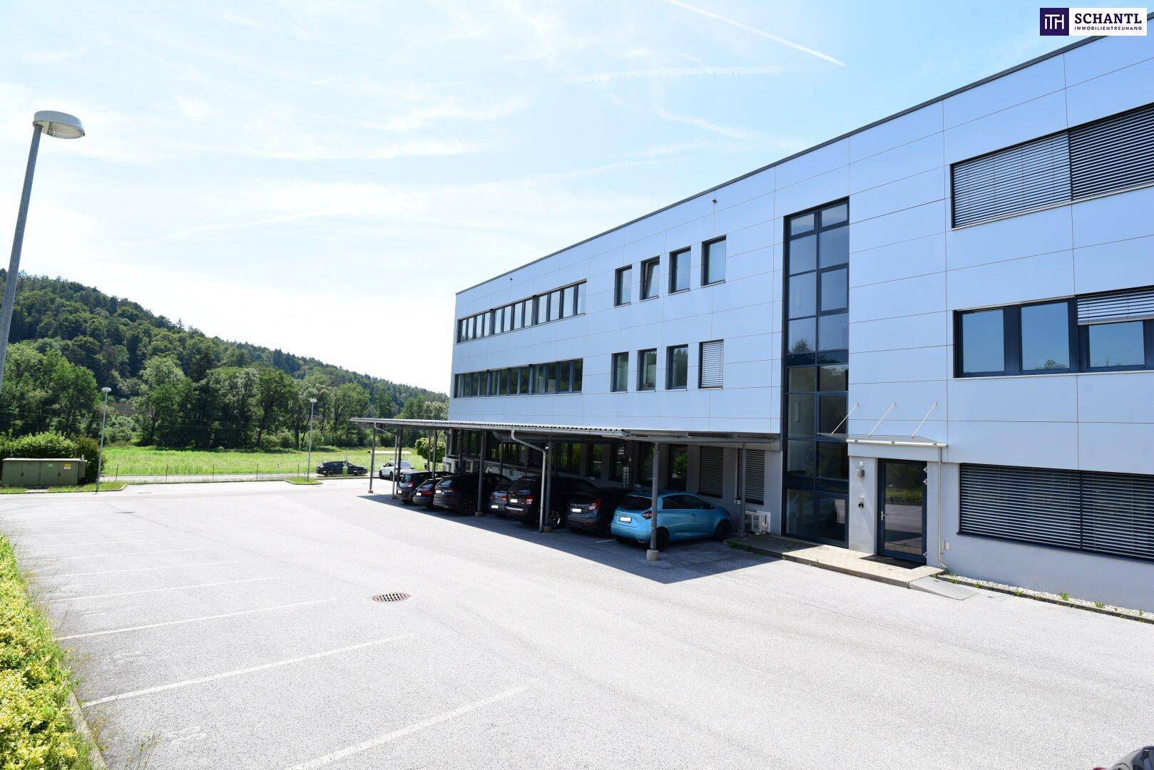 Modernes Bürogebäude mit überdachten Parkplätzen und einem großen, leeren Parkbereich davor.