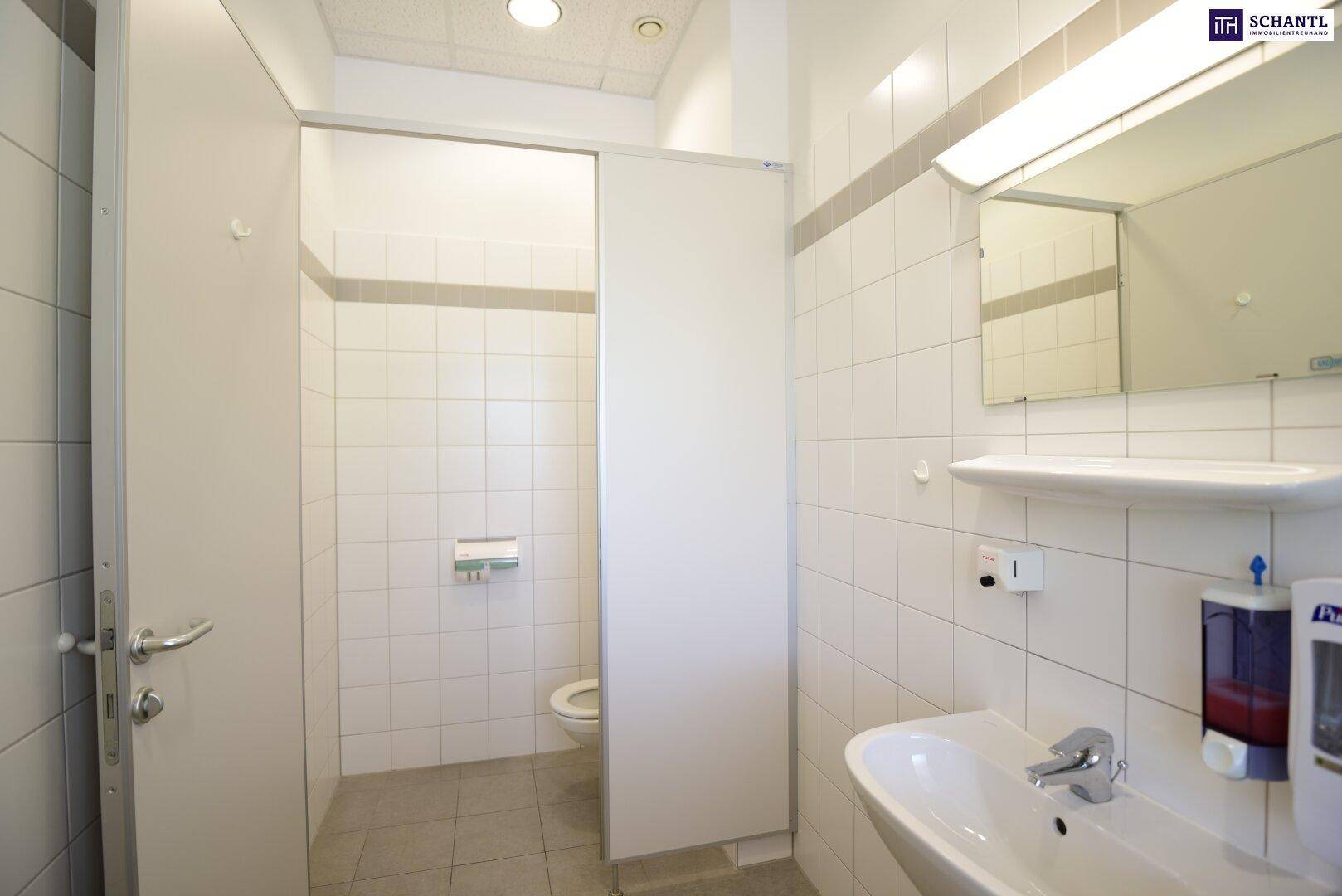 Sauberer öffentlicher Waschraum mit weißen Fliesen, mehreren Toilettenkabinen und einem Waschbecken.