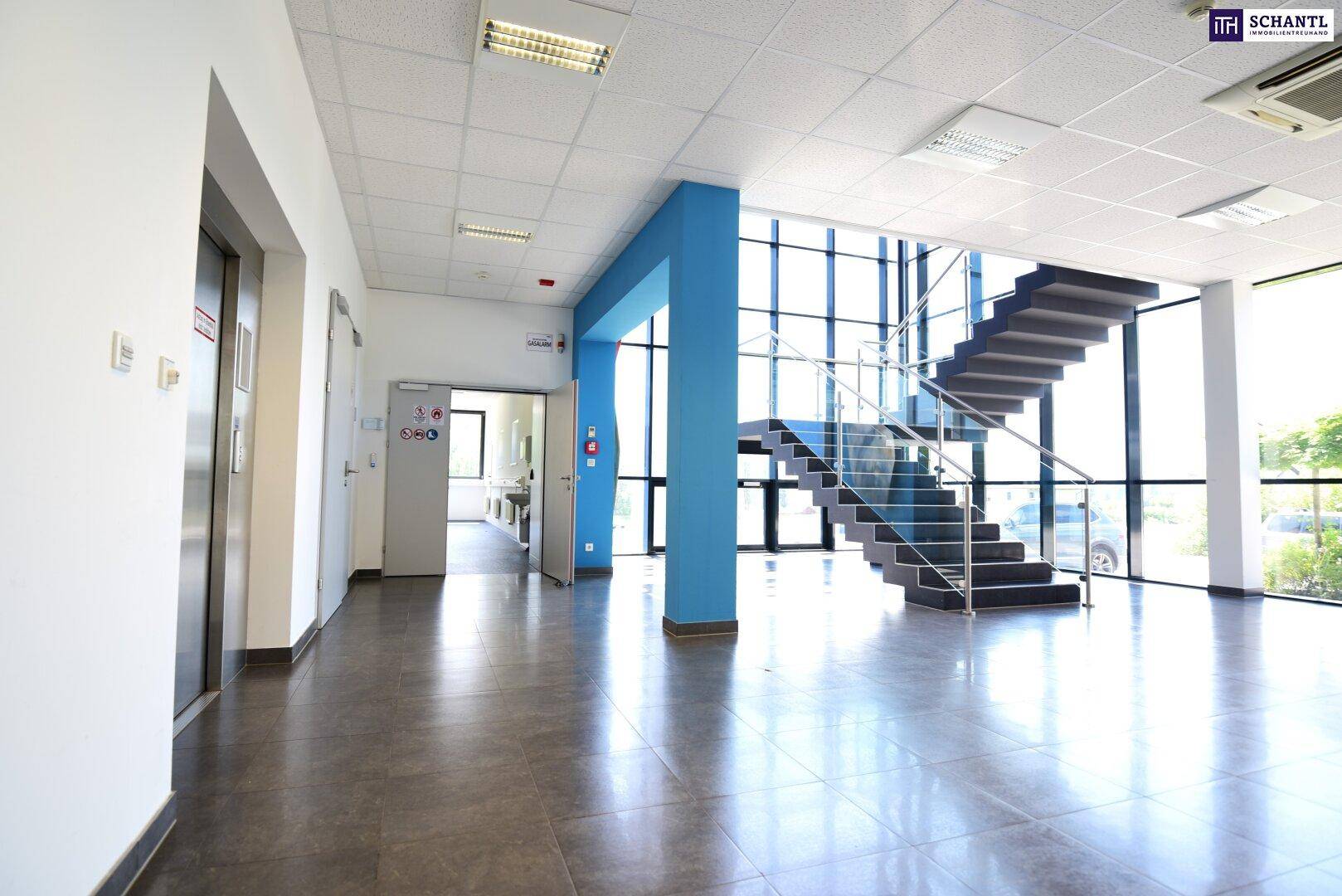 Heller Eingangsbereich mit moderner Treppe, großen Fenstern und Fliesenboden.