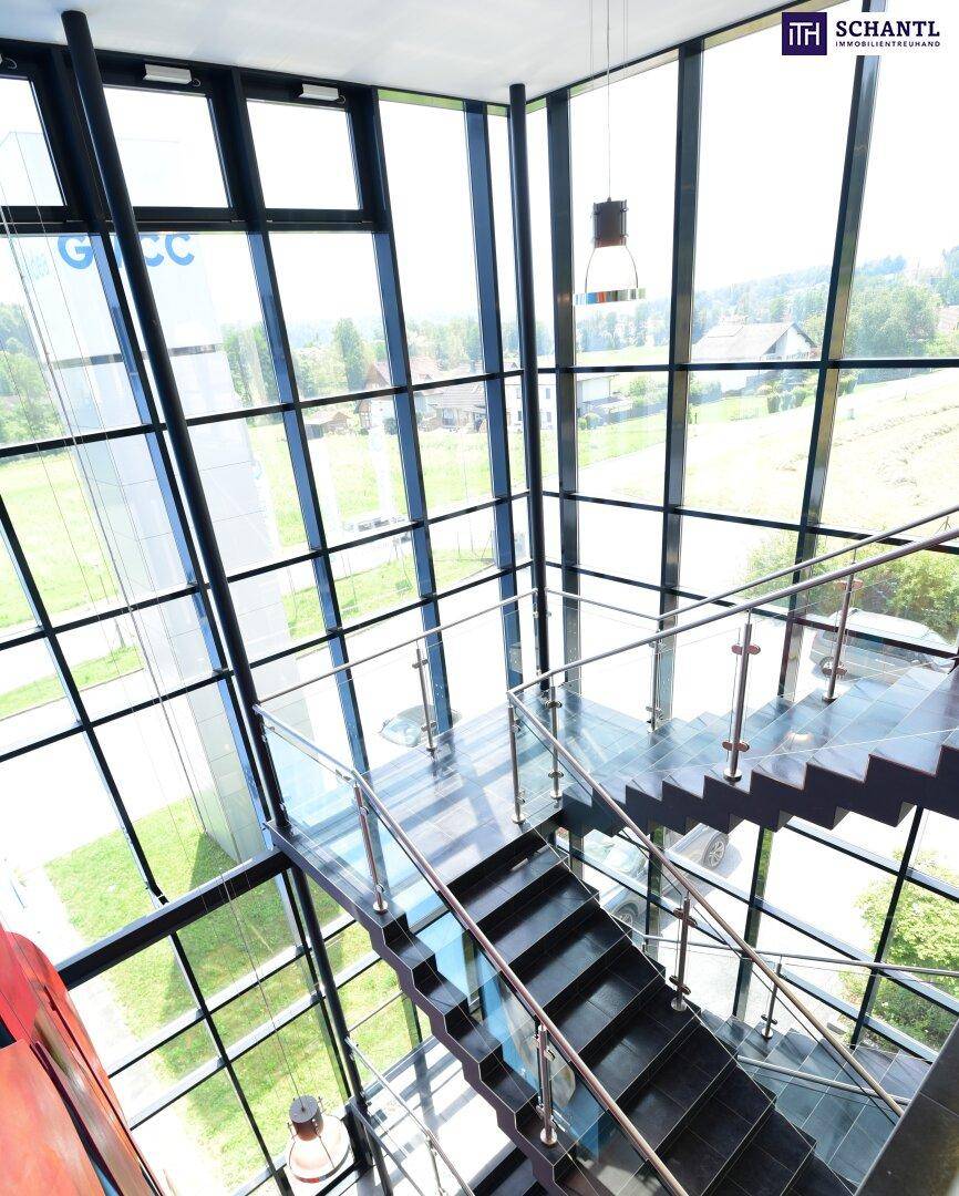 Moderne Treppe mit Glasgeländer und großen Fensterfronten, die einen weiten Blick in die Umgebung ermöglichen.