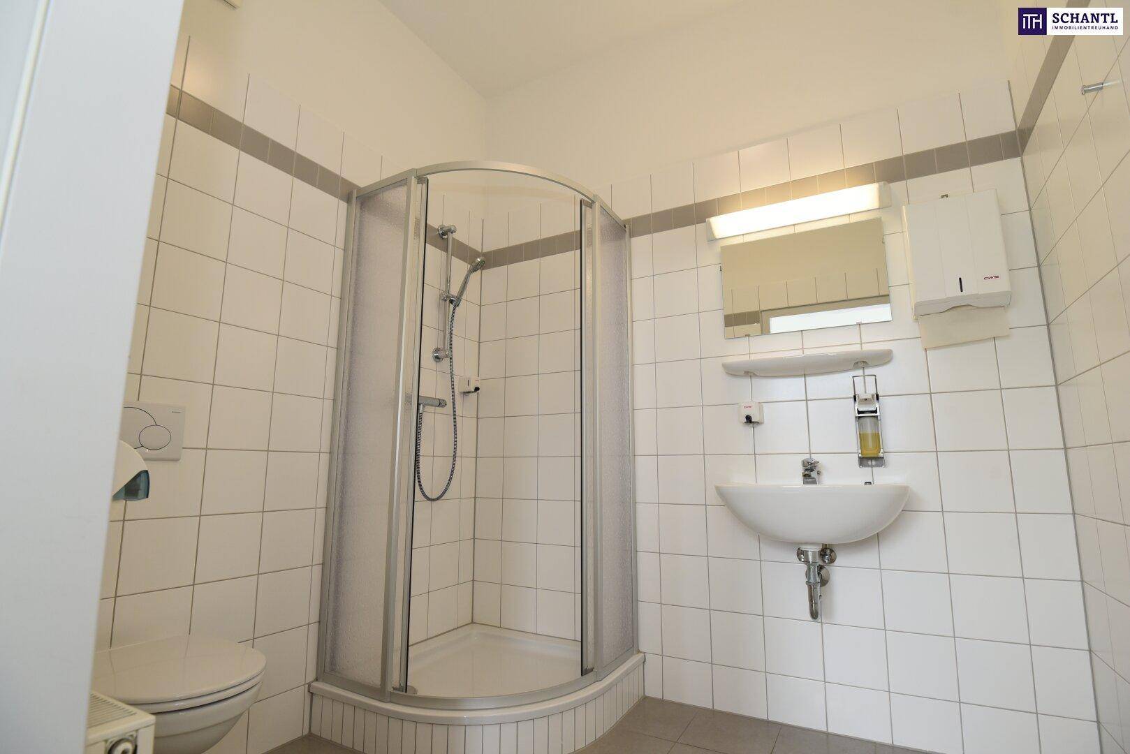 Badezimmer mit weißen Fliesen, Waschbecken, Spiegel und einer runden Duschkabine, in gutem Zustand.