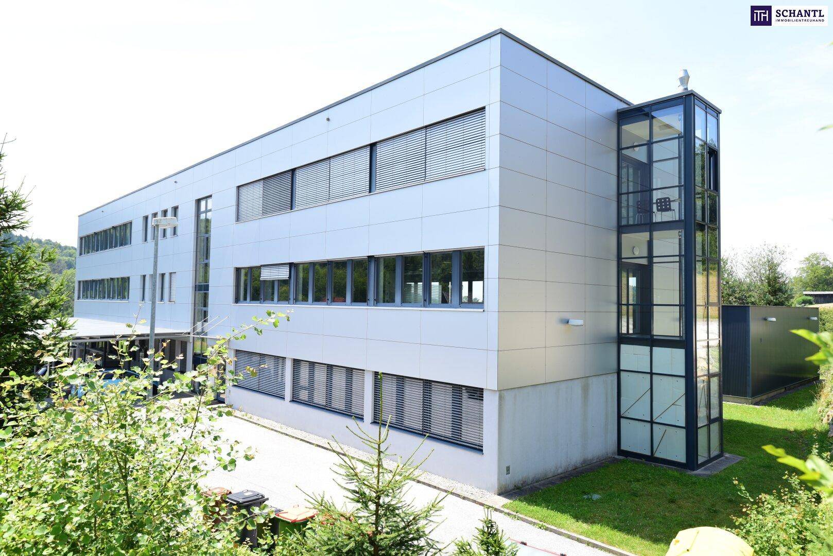 Seitenansicht des modernen Bürogebäudes mit externem Glasaufzug und schlichten Fassadenplatten.