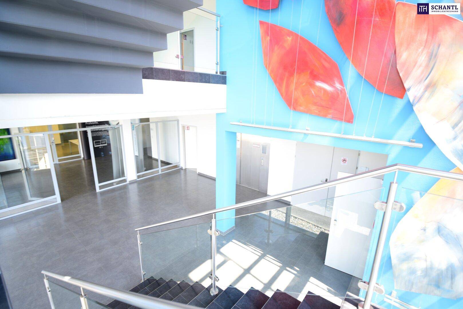 Helle Eingangshalle mit moderner Treppe, Glasgeländer und farbenfroher Wandgestaltung, einladend und offen.