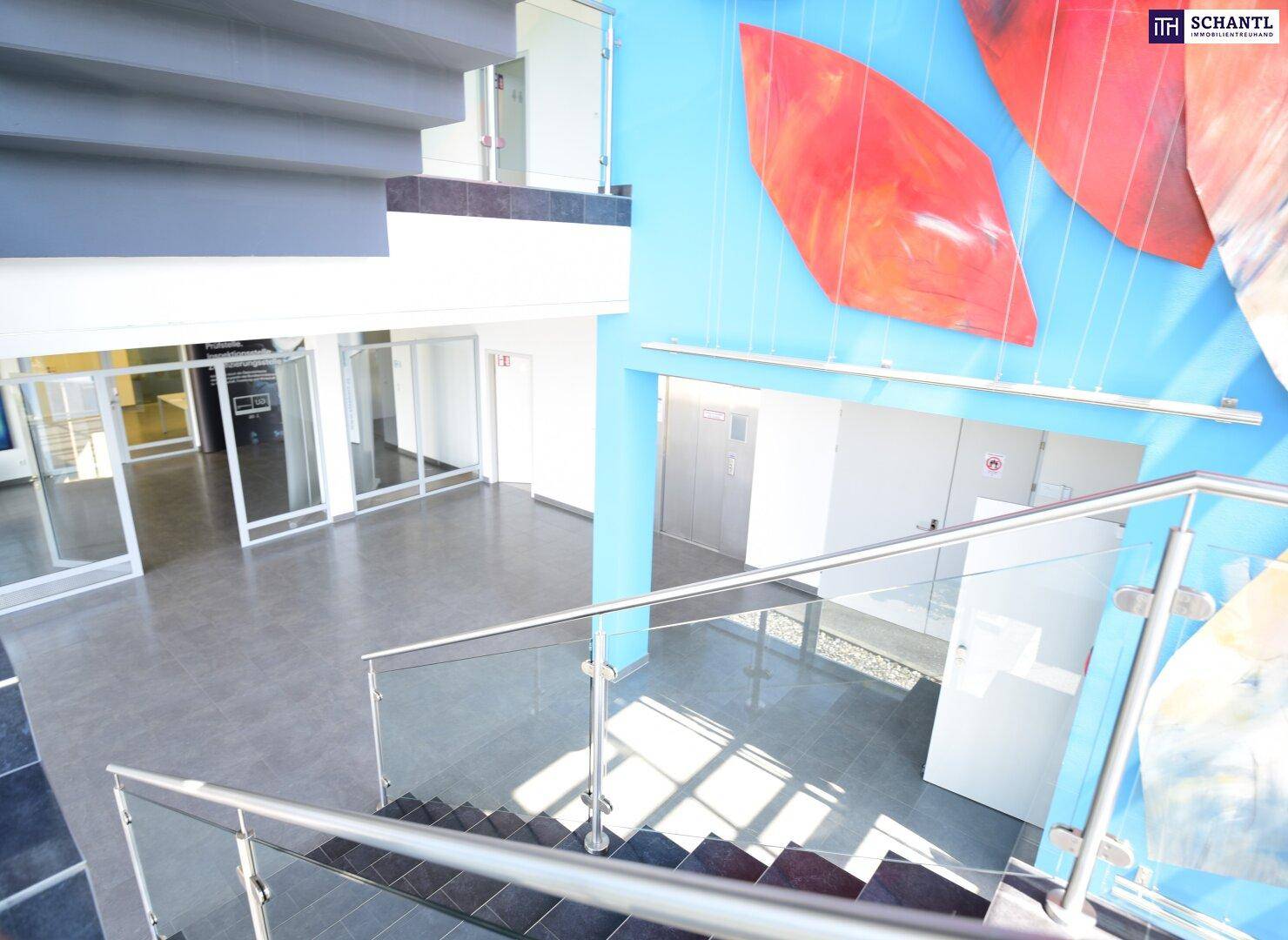 Heller Treppenaufgang mit Glasgeländer und Kunstinstallation, der verschiedene Etagen verbindet.