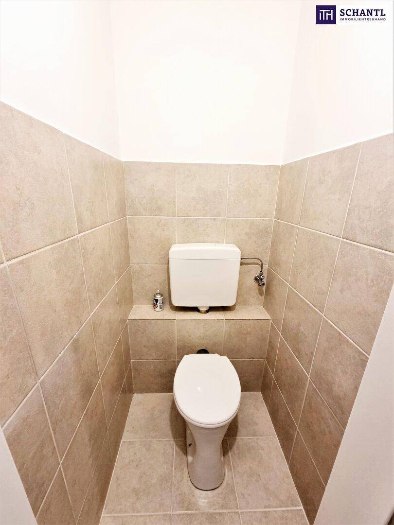 Separate Toilette mit beigefarbenen Fliesen und wandmontiertem Spülkasten, sauber und funktional.