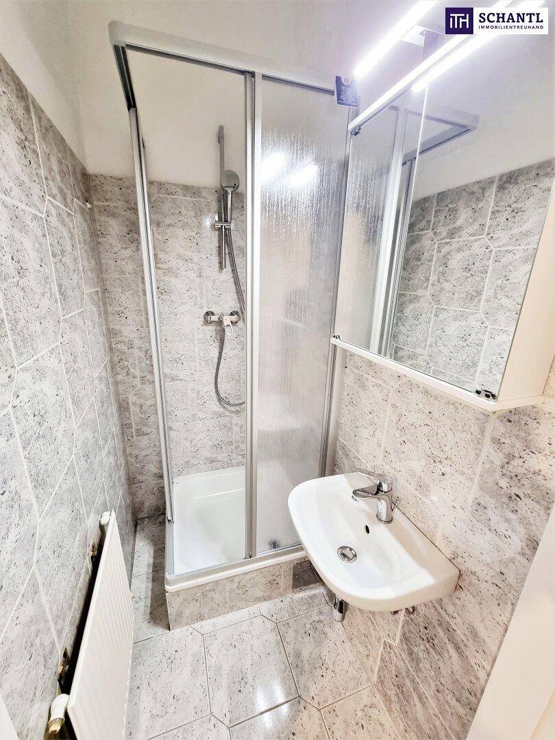 Kleines Badezimmer mit Duschkabine, Waschbecken und grauen Fliesen, funktional und hell.