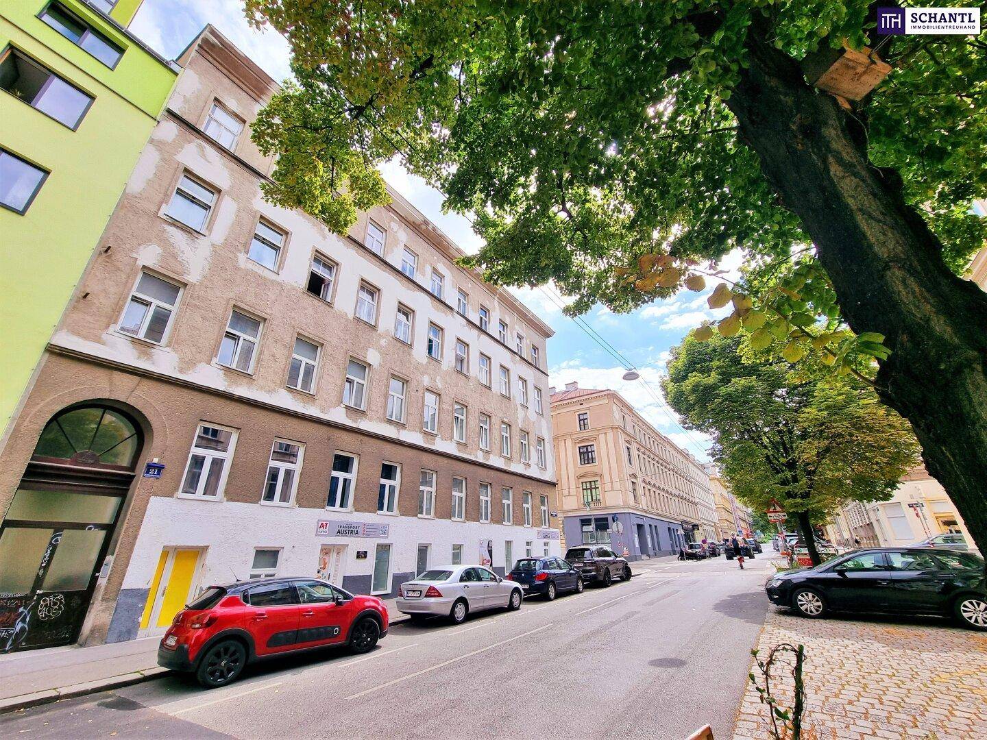 Historisches Gebäude an einer belebten Straße mit Bäumen und parkenden Autos.