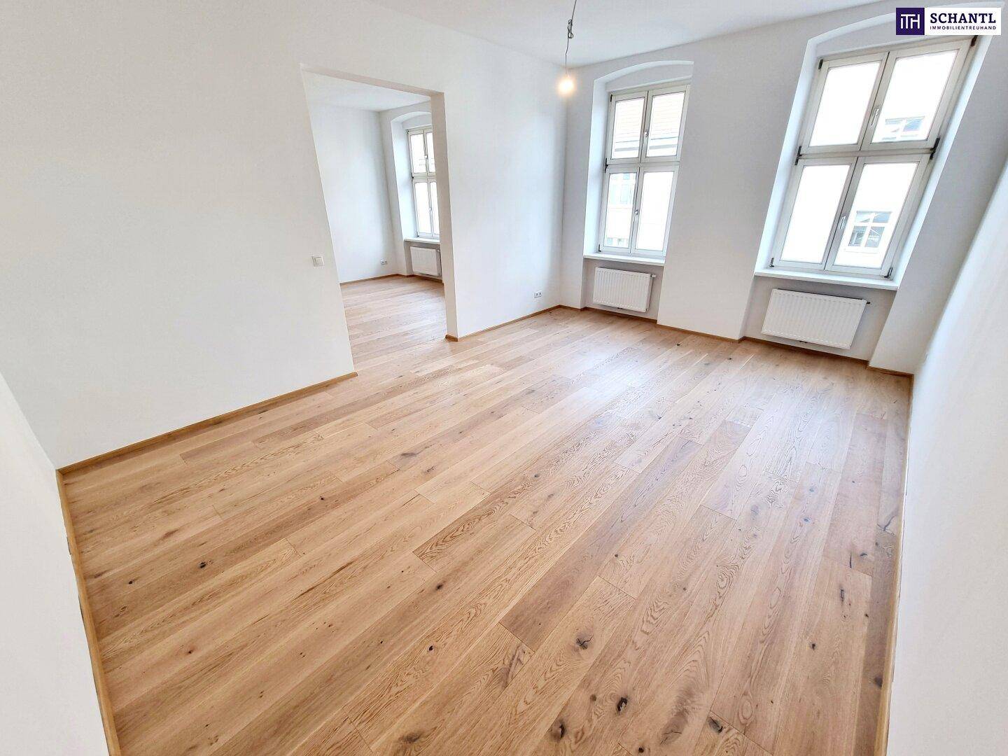 Lichtdurchflutetes Zimmer mit Parkettboden und zwei großen Fenstern.