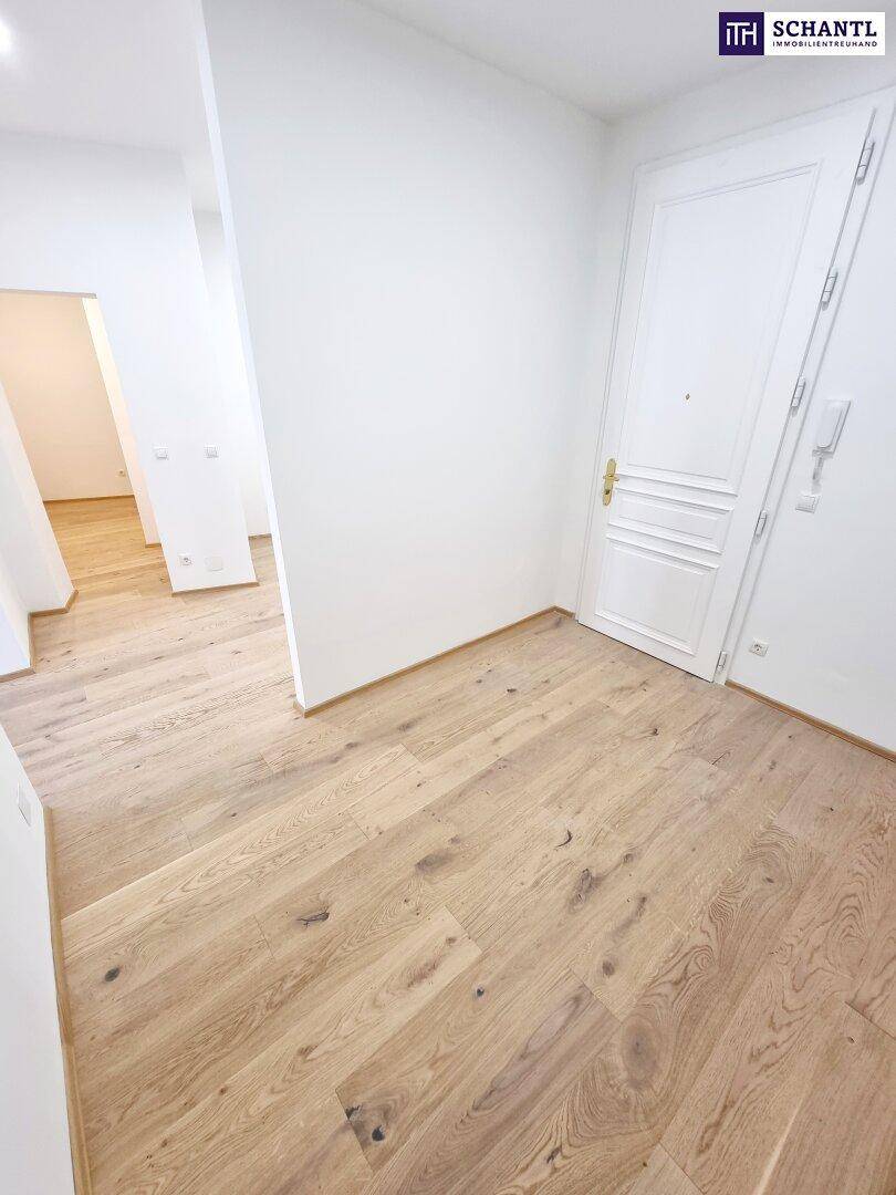 Heller Eingangsbereich mit Parkettboden und weißer Tür, führt zu weiteren Räumen.