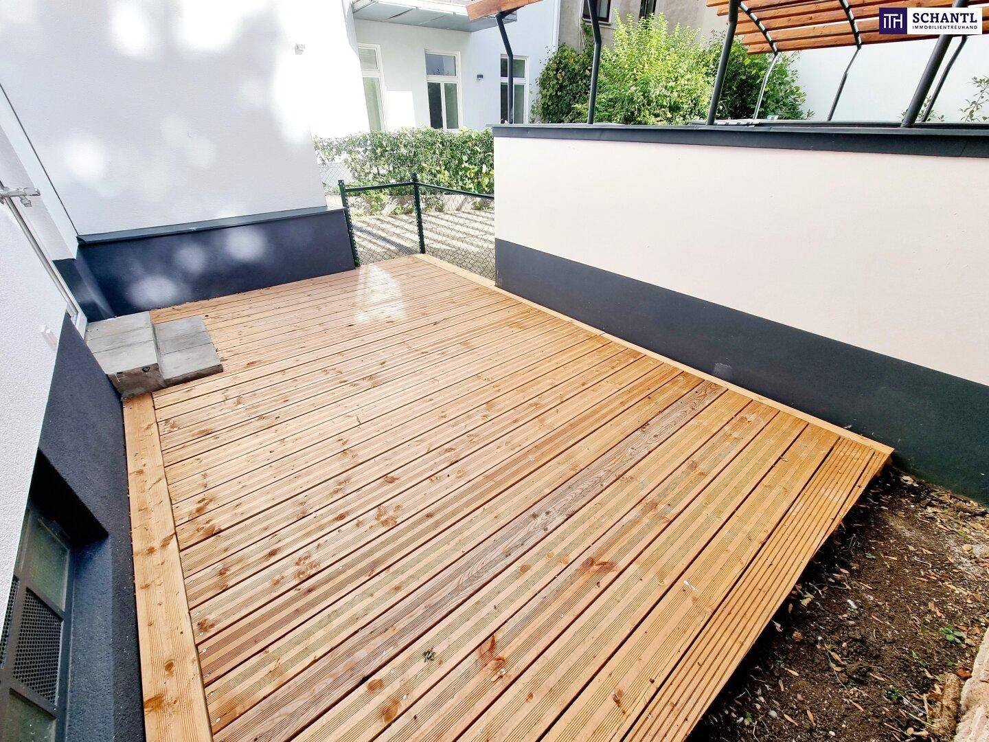 Neu errichtete Holzterrasse im Außenbereich, umgeben von einer niedrigen Mauer.