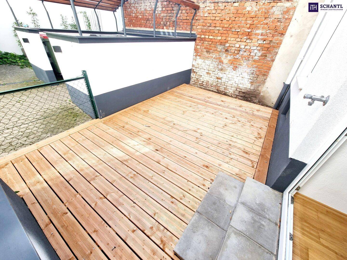 Neu errichtete Holzterrasse mit Stufen zum Innenbereich und angrenzender Ziegelwand.