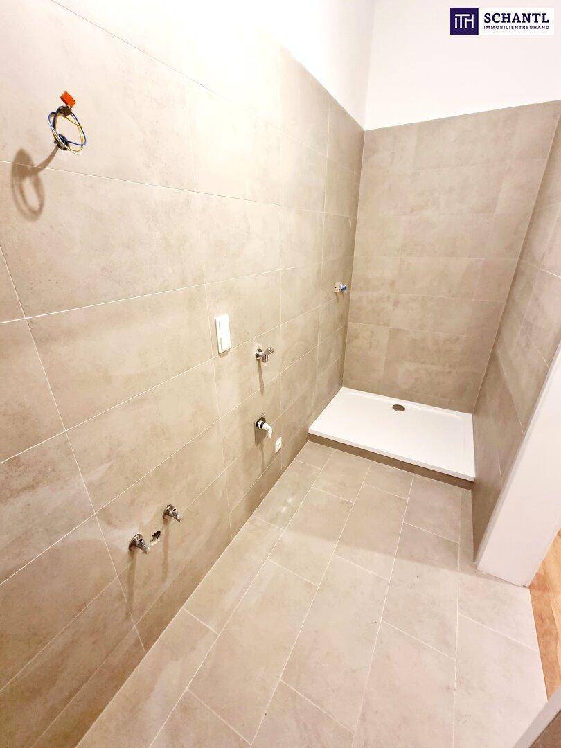 Neu geflieste Dusche mit Duschwanne und modernen Armaturen in einem hellen Badezimmer.