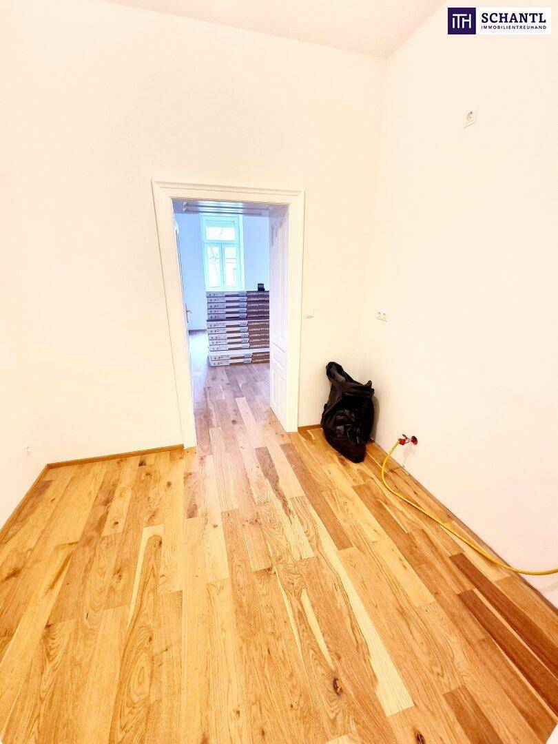 Renovierter Raum mit neuem Parkettboden und offener Tür zu einem weiteren Zimmer.