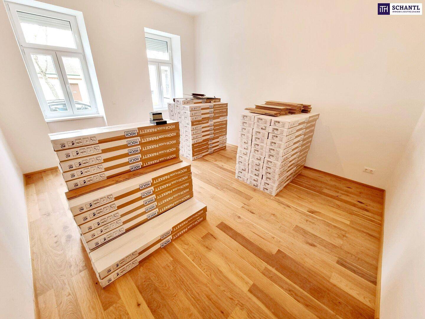 Lichtdurchfluteter Raum mit großen Fenstern und neuem Parkettboden, bereit zur Fertigstellung.