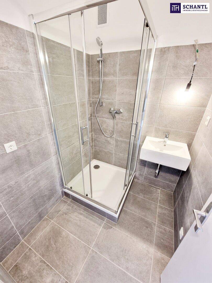 Badezimmer mit Duschkabine, Waschbecken und grauen Fliesen, hell und funktional gestaltet.