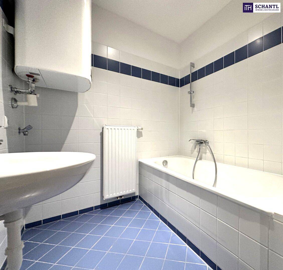 Badezimmer mit Badewanne, Waschbecken und blauen Akzentfliesen, ausgestattet mit einem Warmwasserboiler.