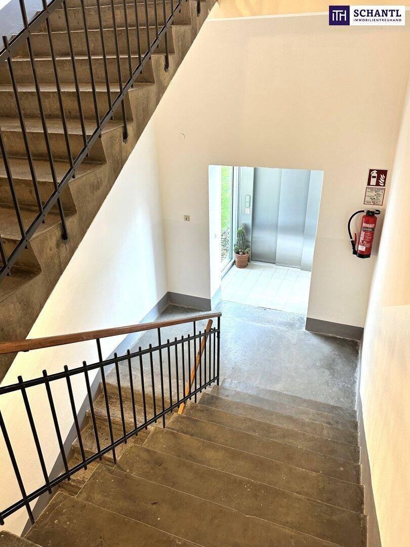 Treppenhaus mit Betonstufen und Metallgeländer, das zu einem modernen Aufzug führt.