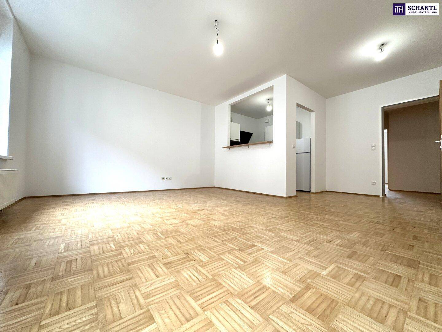 Helles Wohnzimmer mit Parkettboden und einer halb offenen Küchennische, bereit zur individuellen Gestaltung.