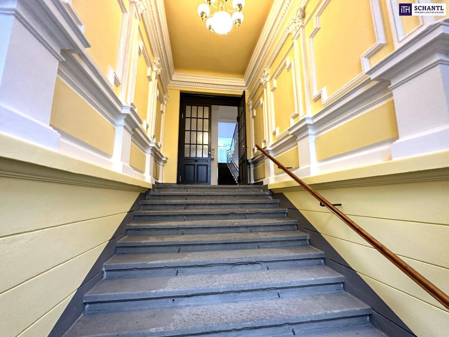 Repräsentatives Treppenhaus mit Stuckverzierungen und gelben Wänden, das den Charme eines Altbaus widerspiegelt.