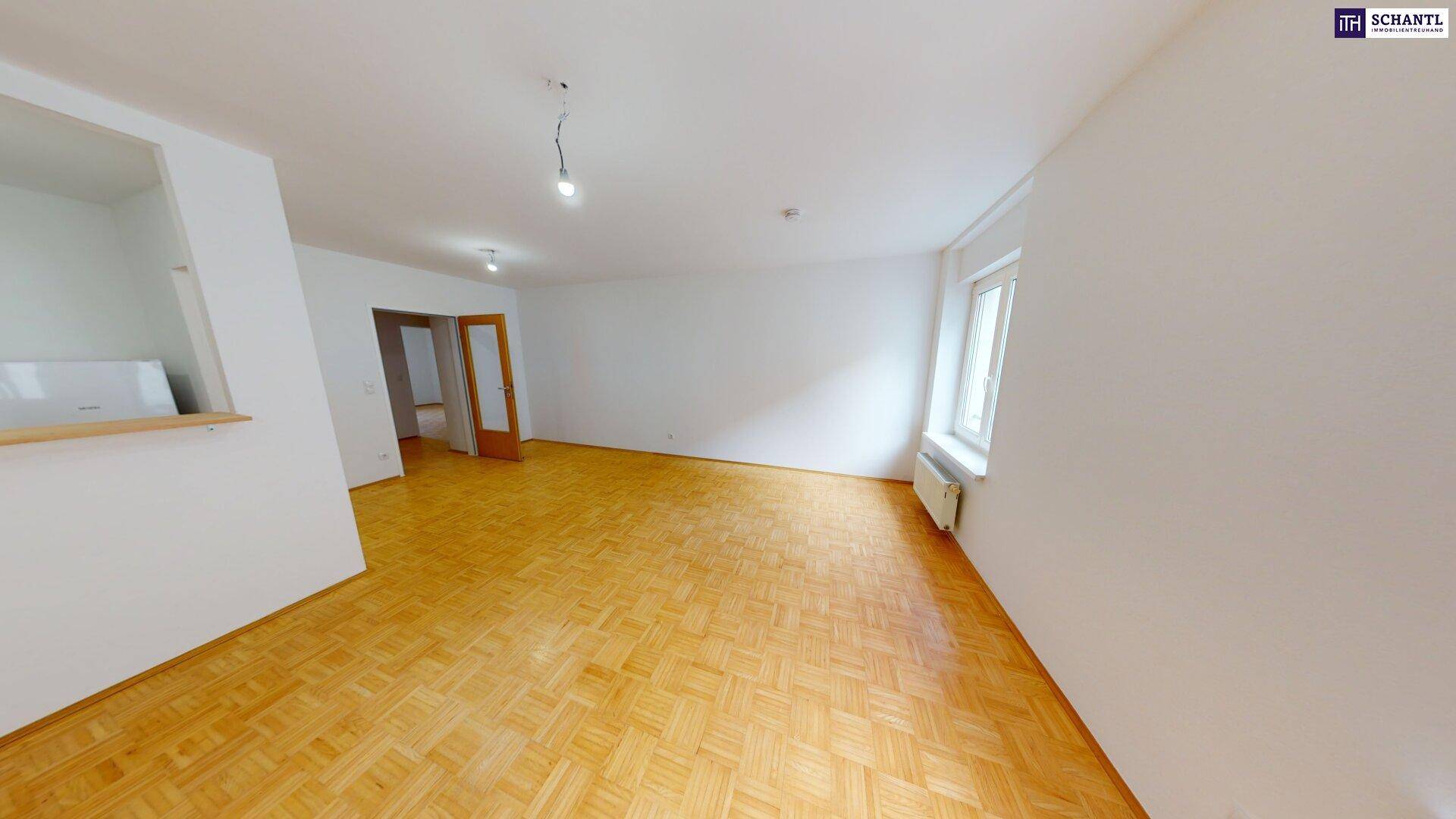 Geräumiges Wohnzimmer mit hellem Parkettboden und großen Fenstern, die viel Tageslicht hereinlassen.