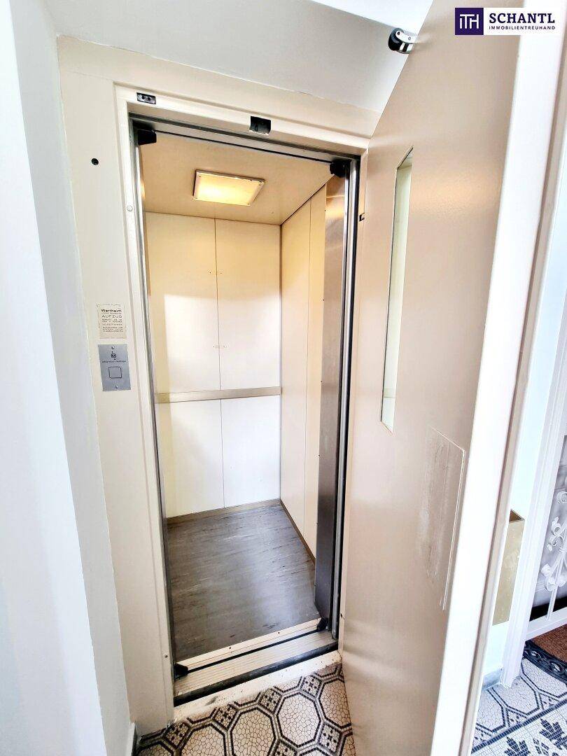 Kleiner, moderner Aufzug in einem historischen Gebäude mit Holzboden und Metallakzenten.