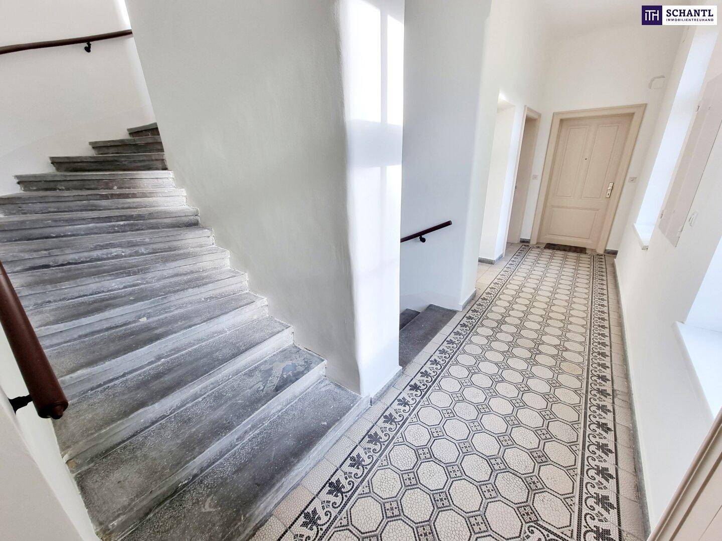 Treppenhaus und Flur eines Altbaus mit originalen Fliesenböden und einer Steintreppe.