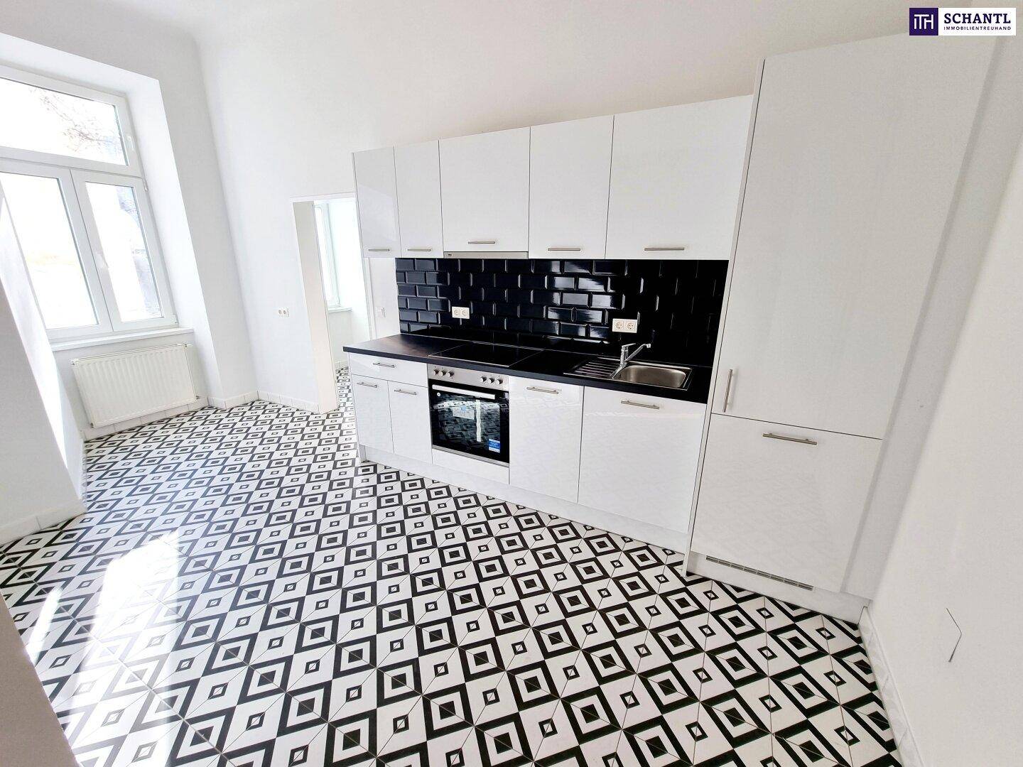 Moderne Küche mit weißen Schränken, schwarzer Arbeitsplatte und gemusterten Bodenfliesen.