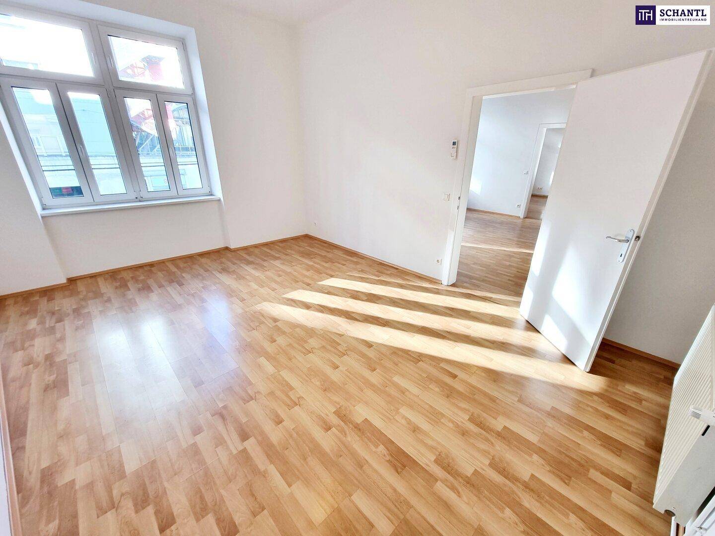Geräumiges Zimmer mit Laminatboden, weißen Wänden und großen Fenstern, die viel Licht hereinlassen.