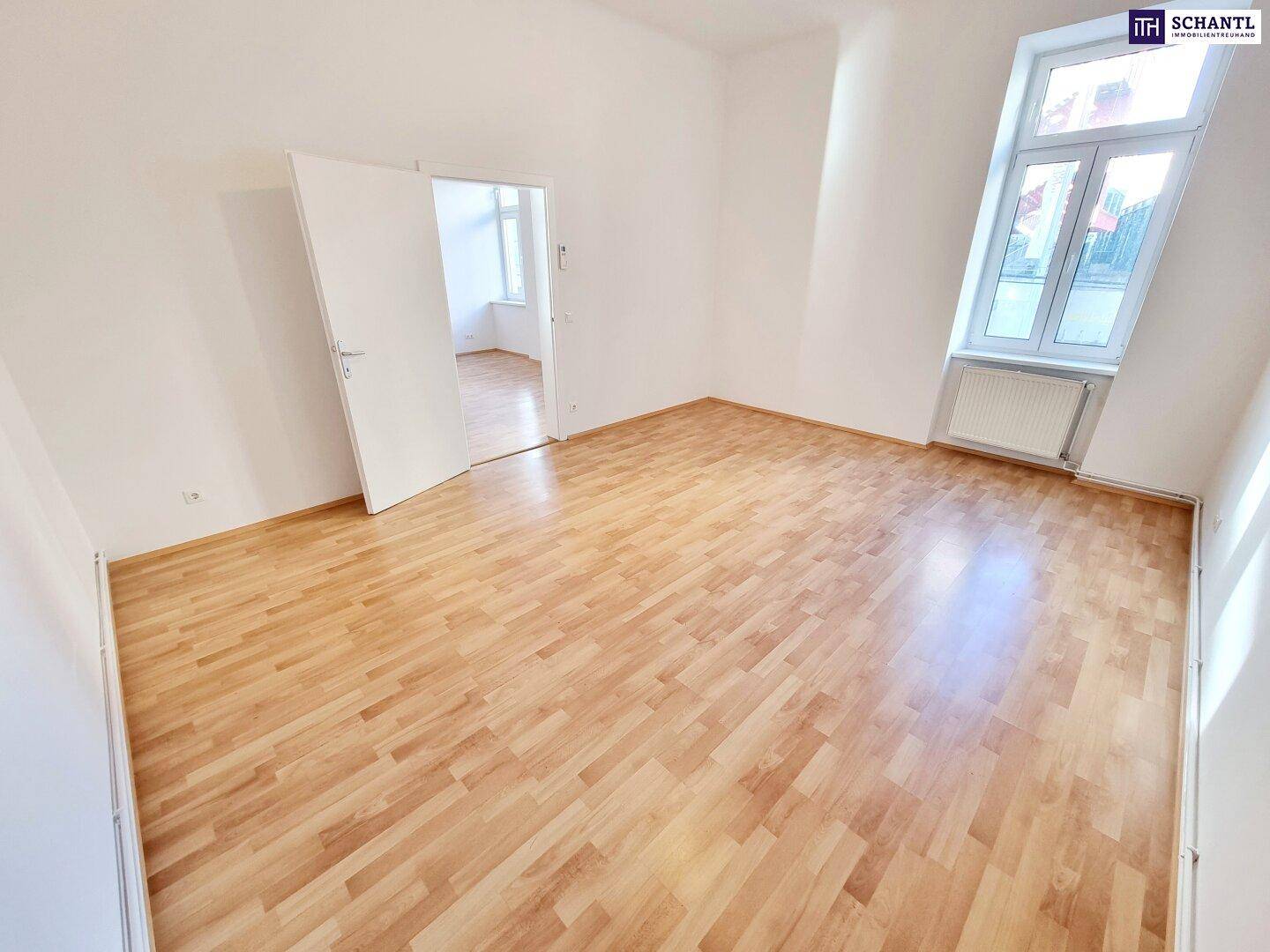 Geräumiges Zimmer mit Laminatboden, weißen Wänden und großen Fenstern.