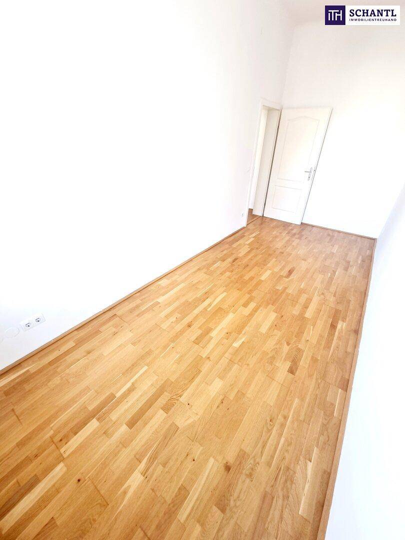 Langer, schmaler Raum mit Parkettboden und weiß gestrichenen Wänden.