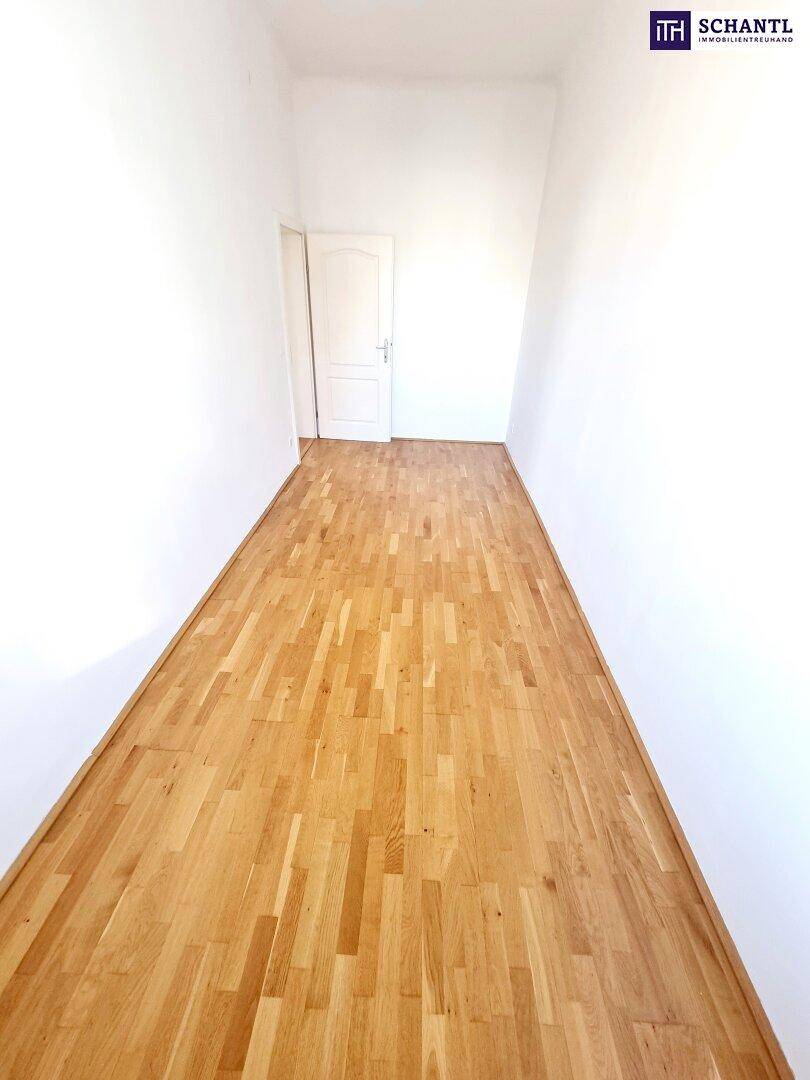 Schmaler Raum mit Parkettboden und weiß gestrichenen Wänden, bietet Zugang zu einem weiteren Bereich.