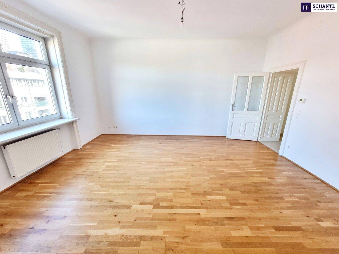 Großes, helles Wohnzimmer mit Parkettboden und breitem Fenster, bietet viel Tageslicht.