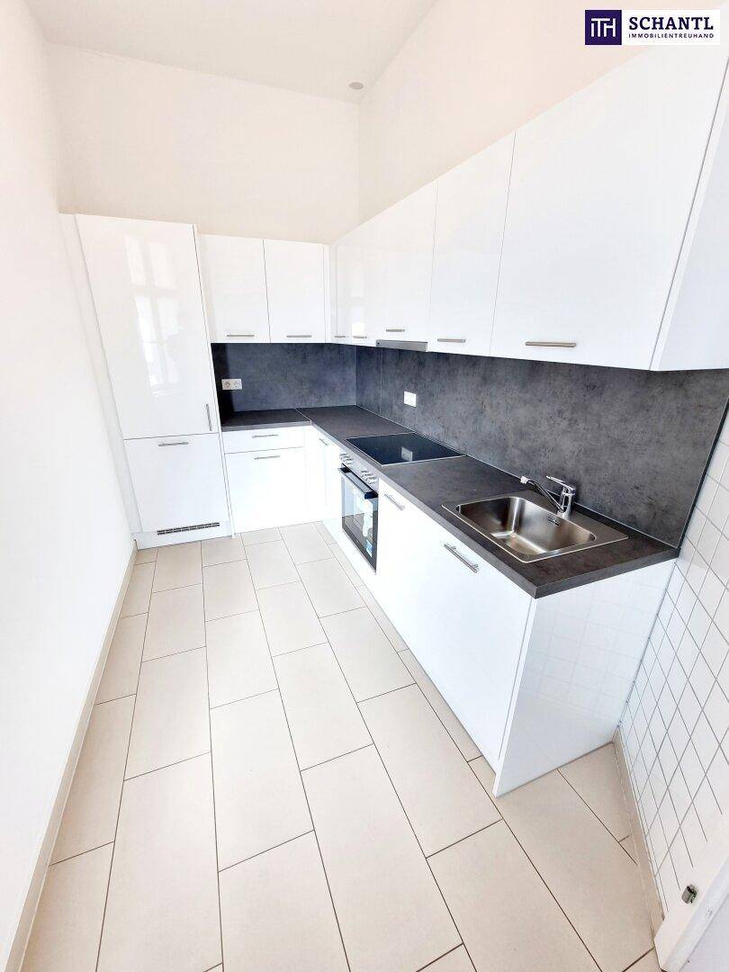 Moderne Einbauküche mit weißen Hochglanzfronten, dunkler Arbeitsplatte und Fliesenboden.