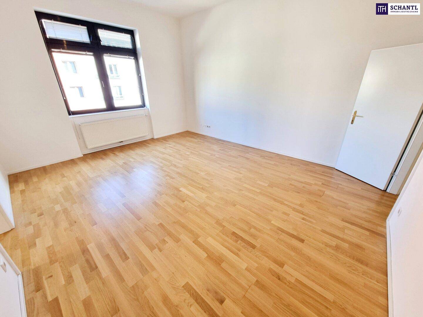 Helles Zimmer mit Parkettboden und großem Fenster, ideal als Wohn- oder Schlafzimmer.