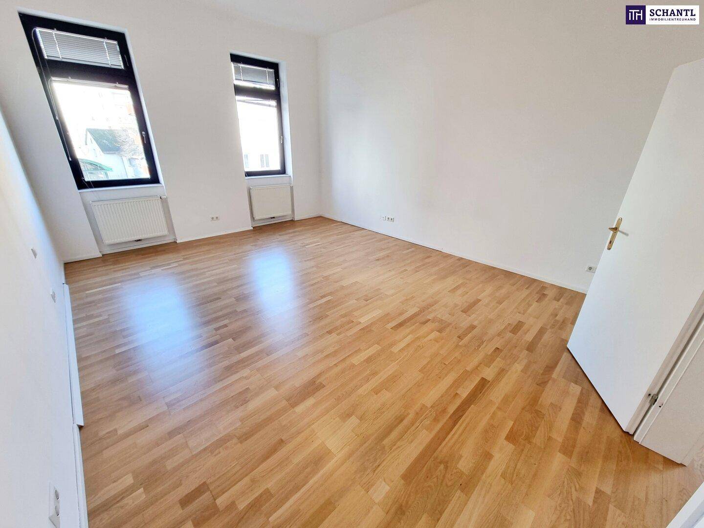 Geräumiges Zimmer mit hellem Parkettboden und zwei Fenstern für viel Licht.