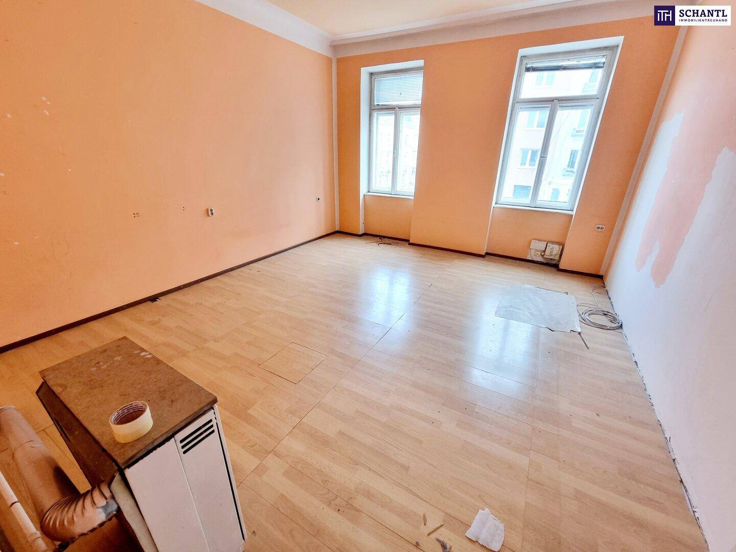 Geräumiges Zimmer mit orangefarbenen Wänden und Laminatboden, bereit zur Renovierung und Neugestaltung.