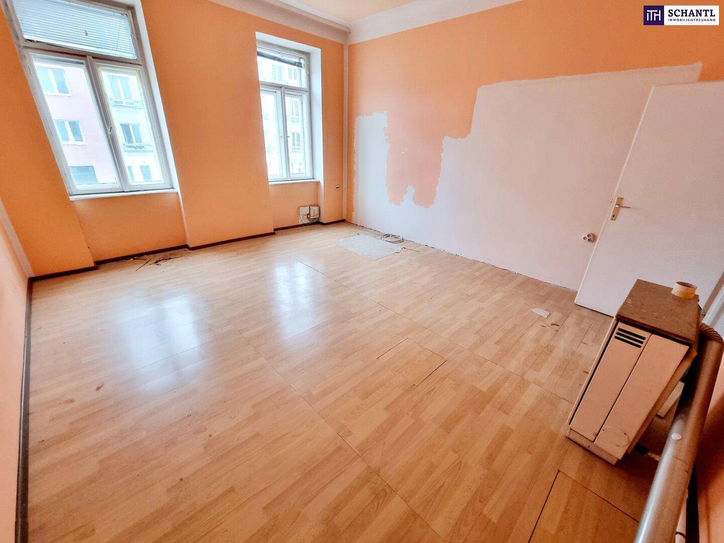Helles Wohnzimmer mit Laminatboden und teilweise gestrichenen Wänden, renovierungsbedürftig.