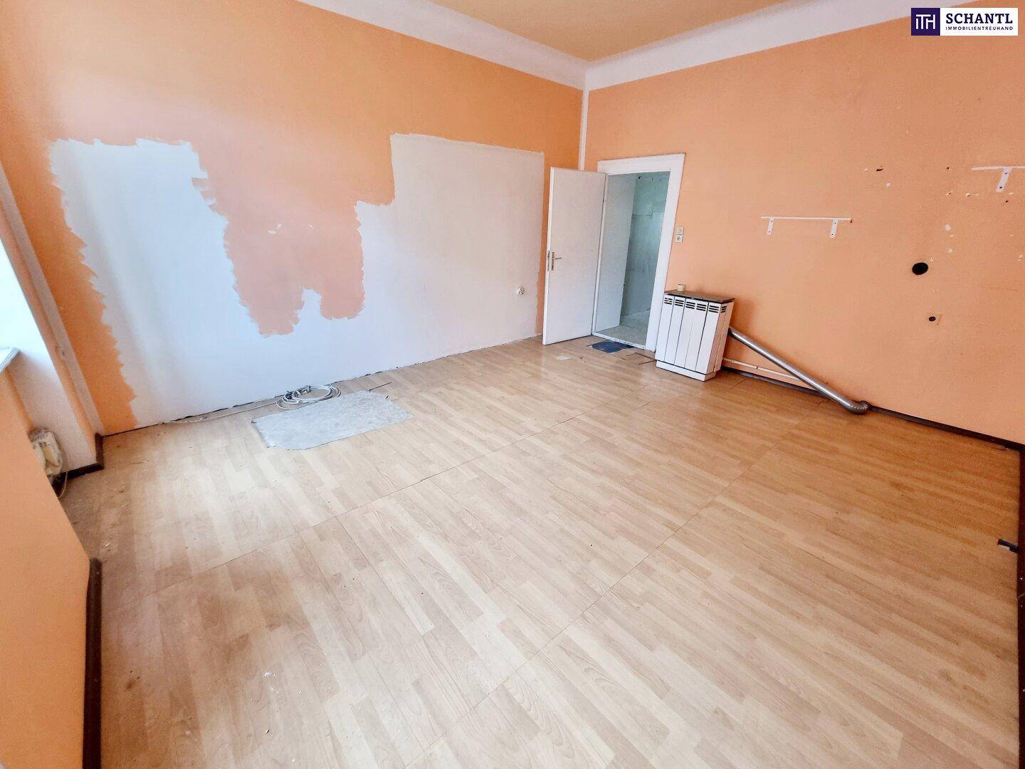 Geräumiges Zimmer mit Laminatboden und orangefarbenen Wänden, bereit für eine Neugestaltung.