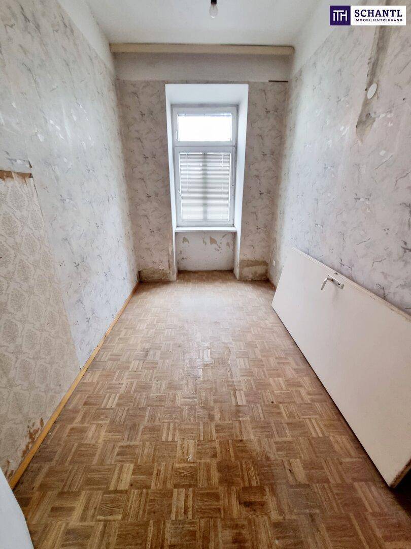 Leeres Zimmer mit altem Parkettboden und einem Fenster, das viel Tageslicht hereinlässt, bereit zur Renovierung.